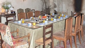 A dining room with a long table set for a meal, surrounded by wooden chairs. A chandelier hangs from the ceiling, and a fireplace is visible in the background. - Manoir du Plessis au Bois (Vauciennes)