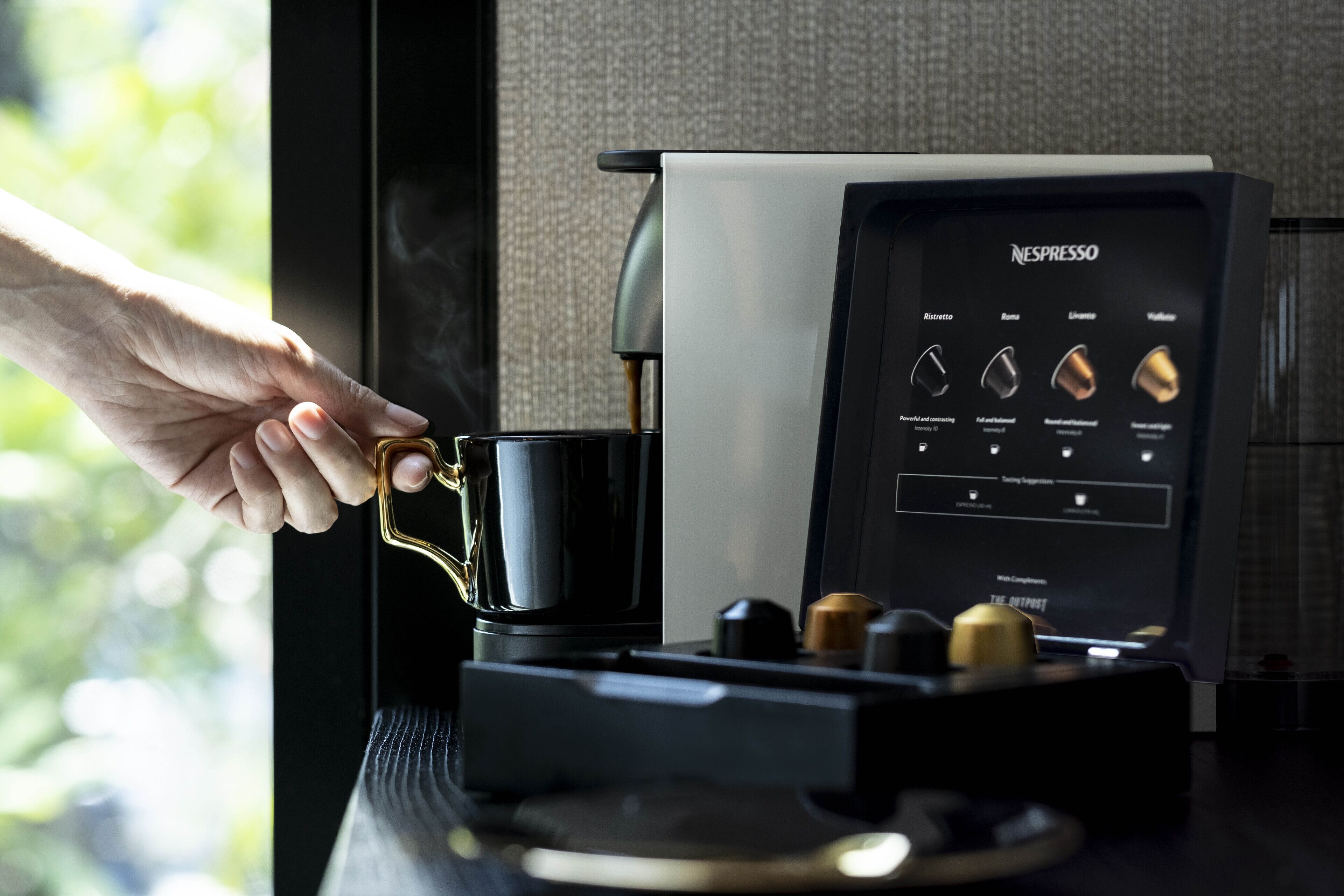 Una mano sostiene una taza de café cerca de una máquina de café Nespresso.
