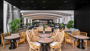 Un restaurante moderno con mesas redondas y sillas de mimbre, una zona de bar y vistas a la ciudad.