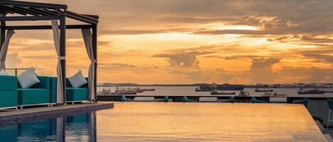 A rooftop pool area with a seating arrangement and a view of the sunset over the water.