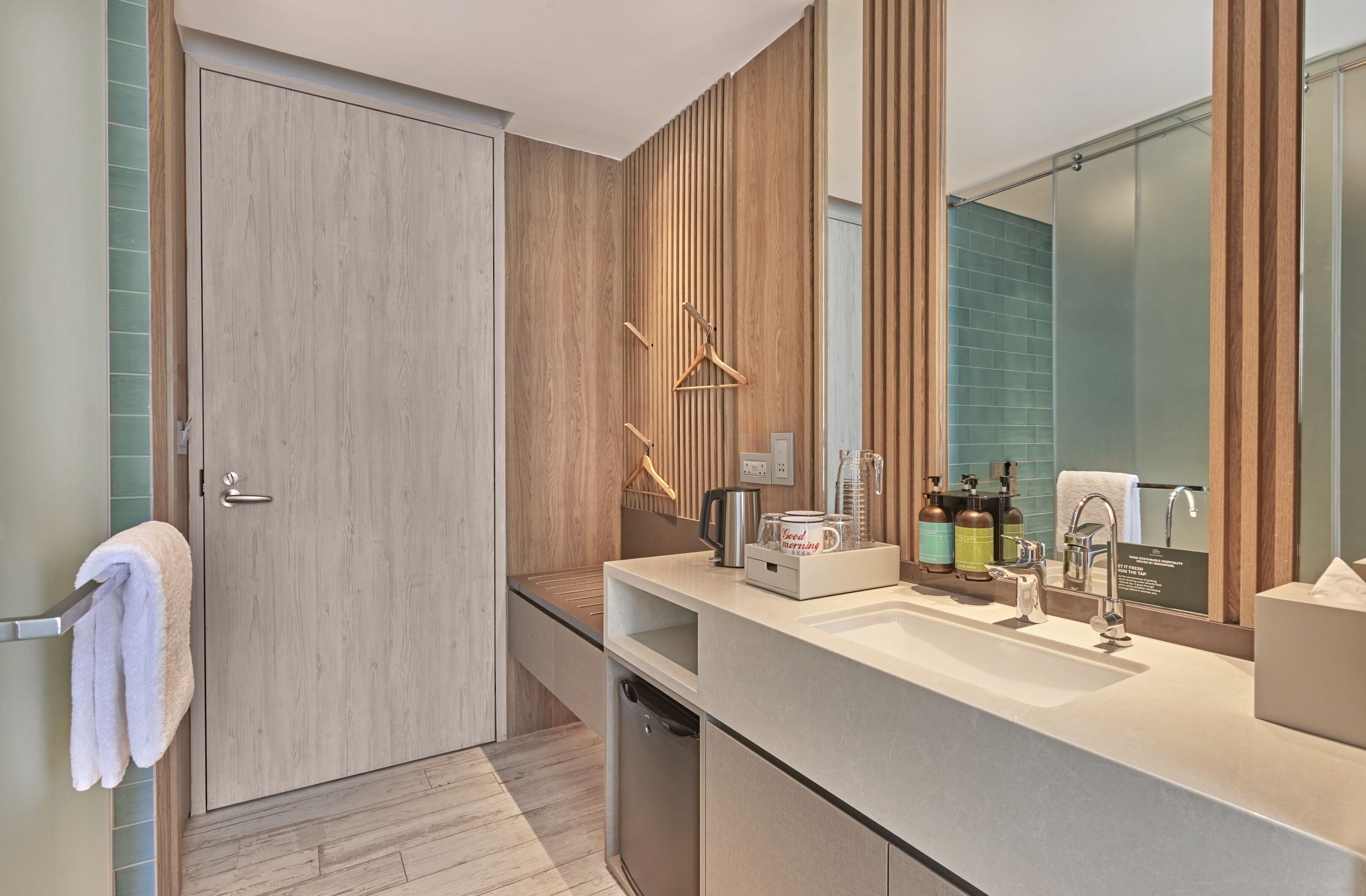 A modern bathroom with a wooden door, a towel rack, a sink with a mirror, and toiletries.