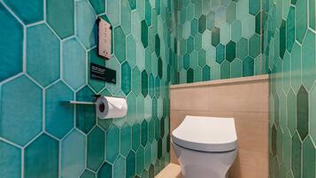 A bathroom with a toilet, a paper towel dispenser, and a sign on the wall.