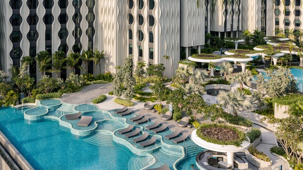 Un hotel moderno con un amplio área de piscina, tumbonas y exuberante jardinería.