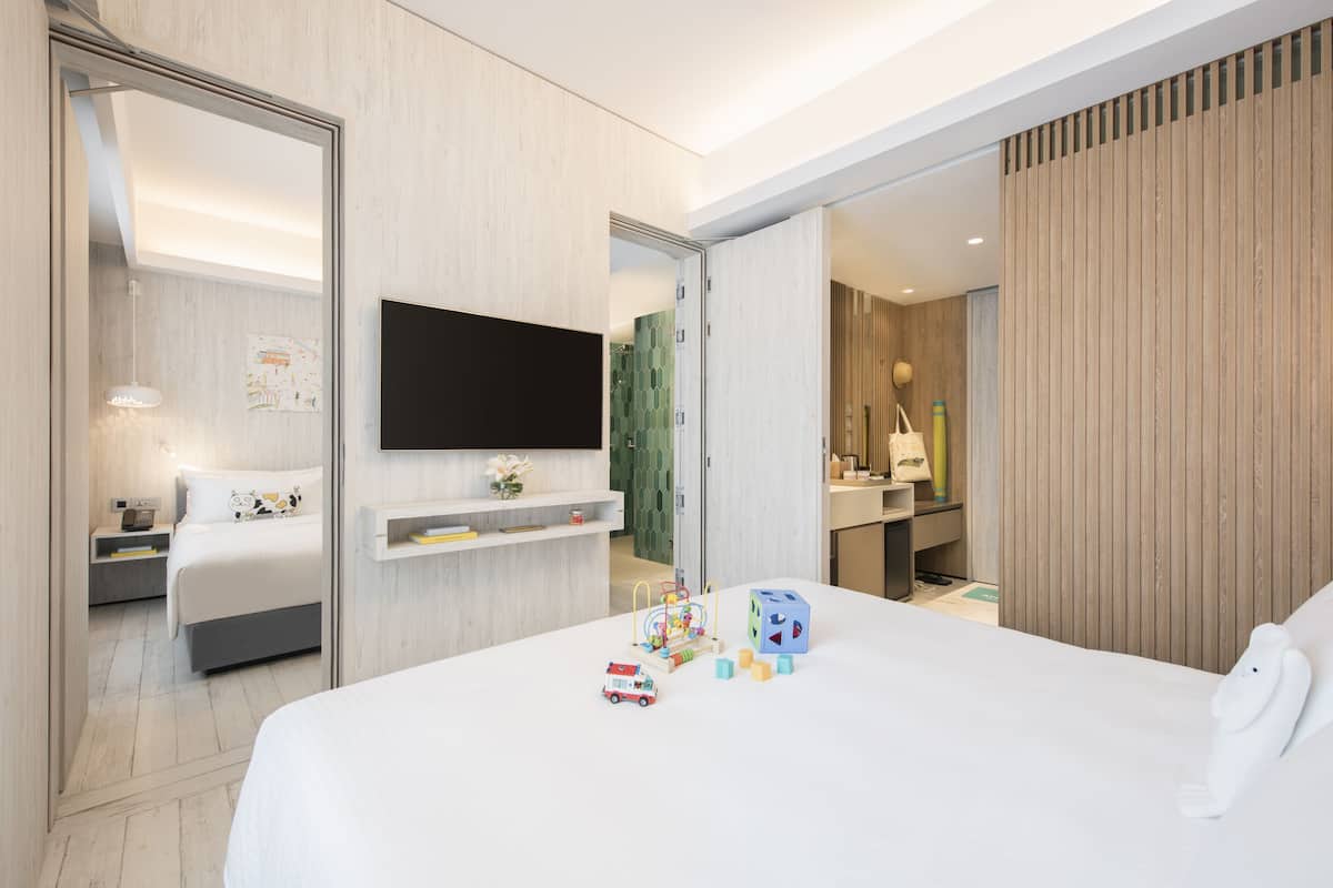 Une chambre d’hôtel moderne dotée d’un grand lit, d’un téléviseur à écran plat, d’une table de chevet avec une lampe et d’un petit espace de jeux avec des jouets.