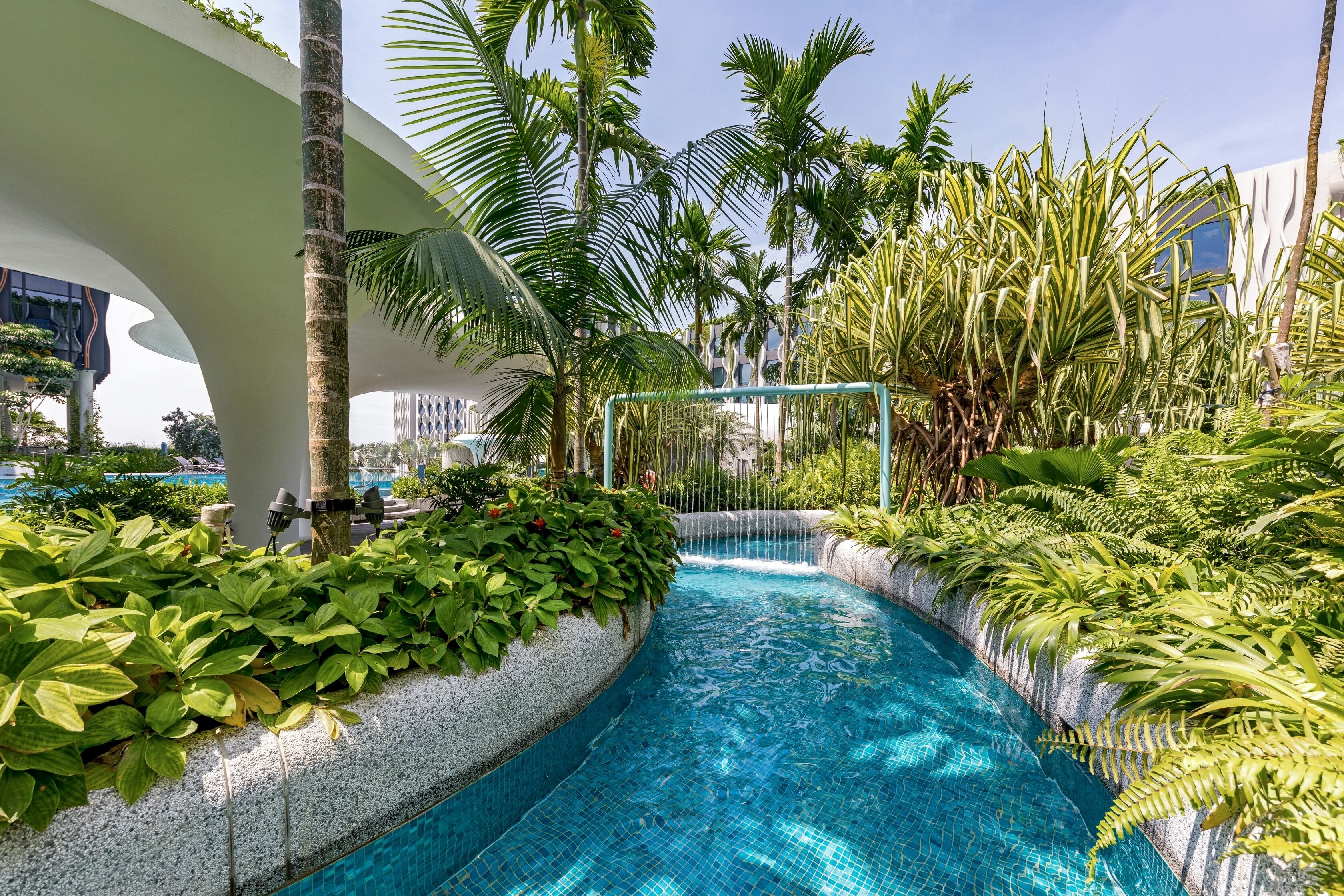 A swimming pool with a waterfall feature, surrounded by lush greenery and modern architecture.