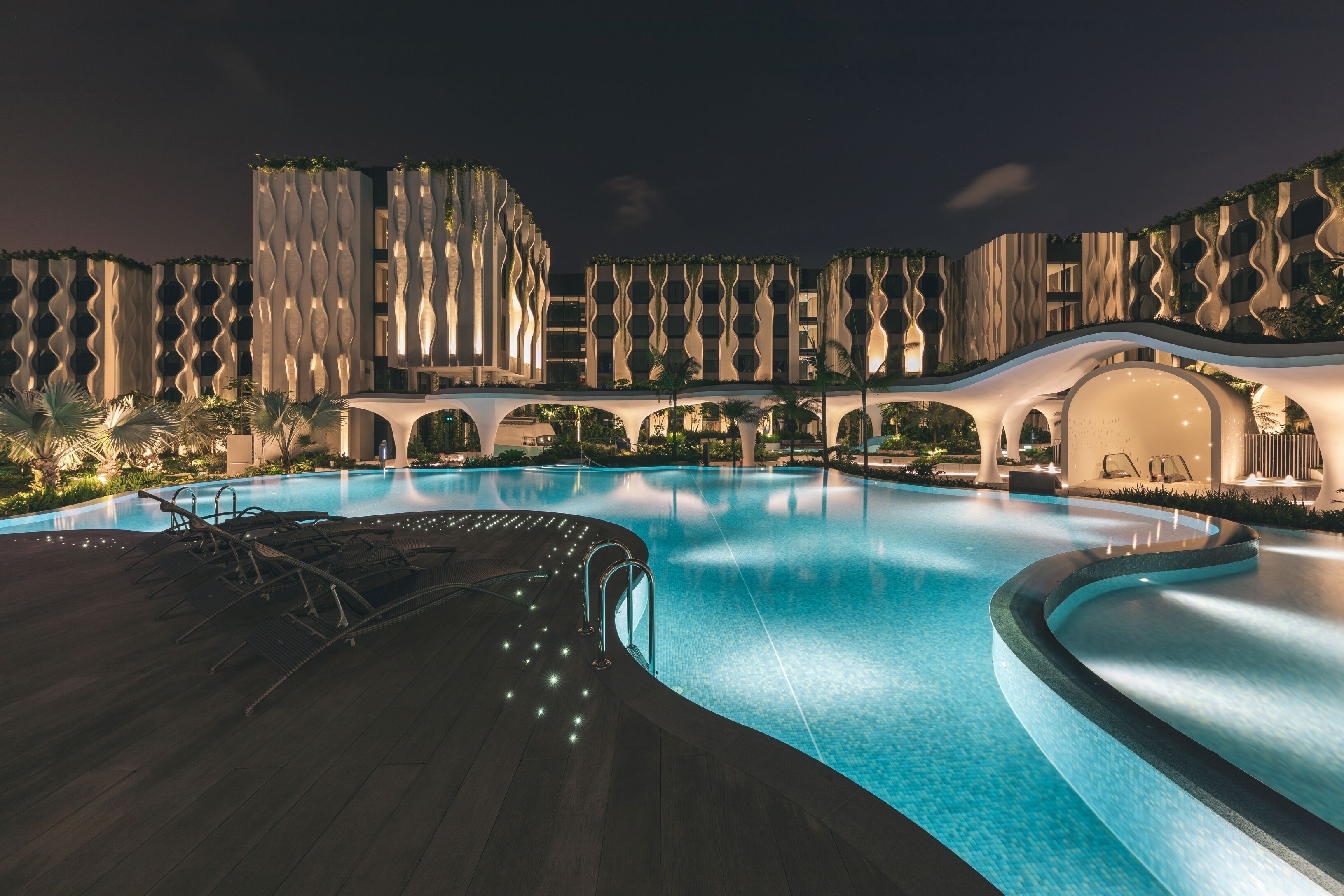 Un hotel moderno con una amplia piscina, diseño arquitectónico ondulado y zonas de estar al aire libre.