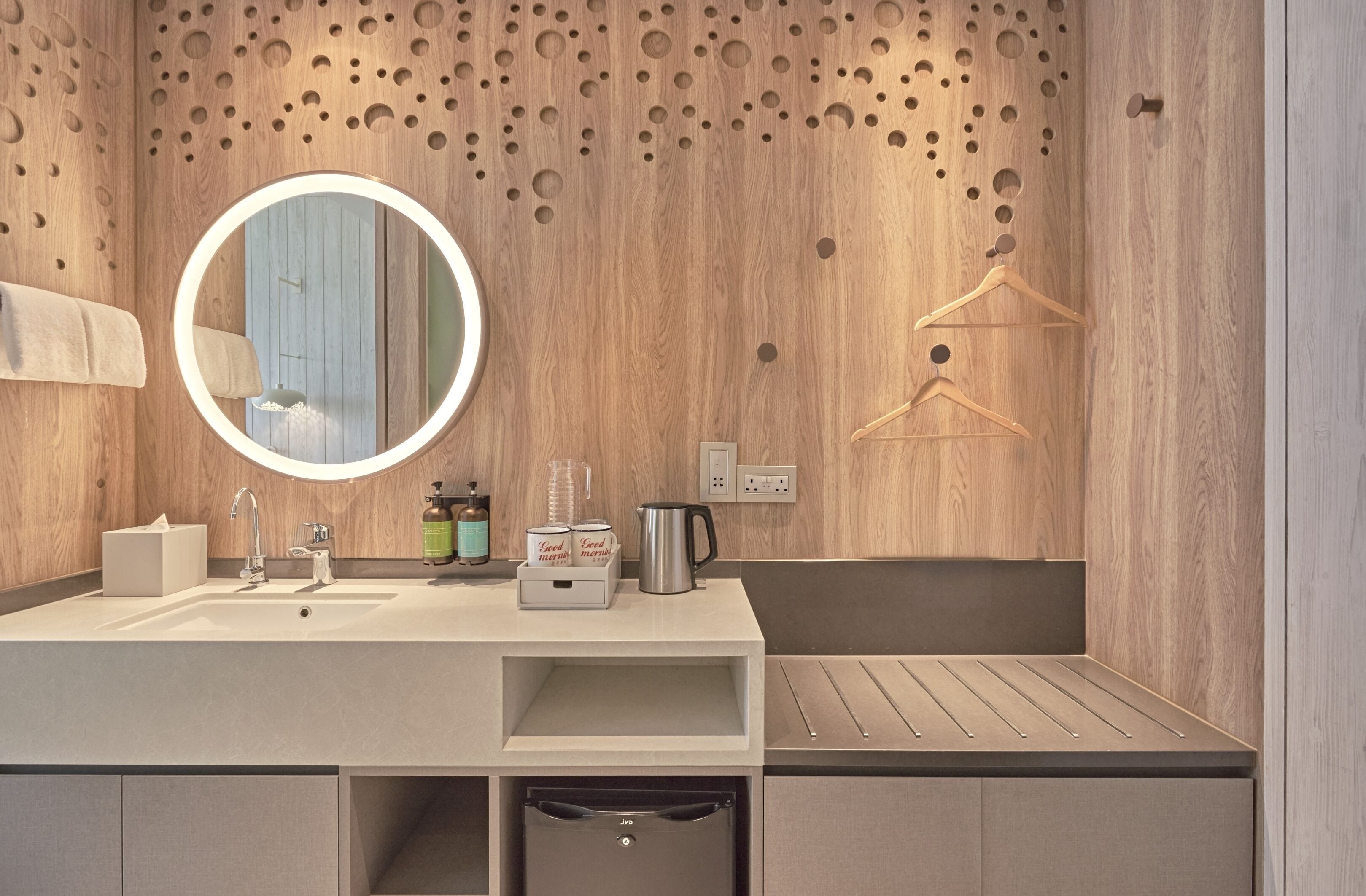 Une salle de bain moderne avec un mur en bois, un miroir rond, un lavabo, une serviette, un distributeur de savon et un luminaire suspendu.