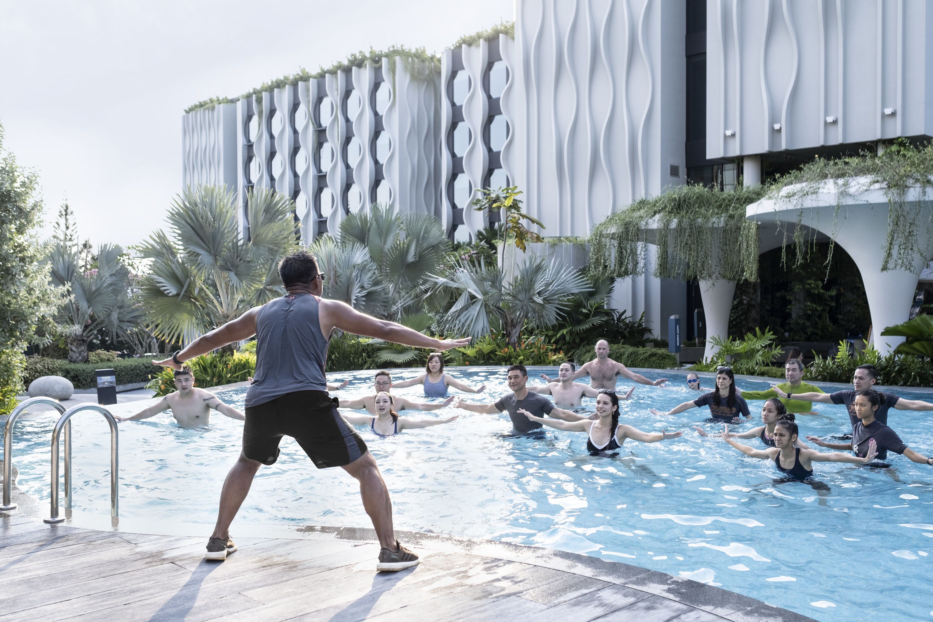 En grupp människor i en swimmingpool med en modern byggnad i bakgrunden.
