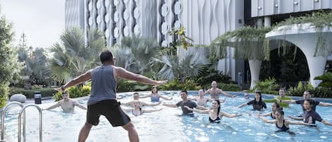 A group of people in a swimming pool with a modern building in the background.