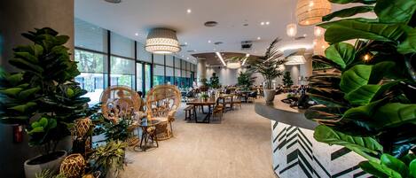 Un hall de hotel espacioso con muebles modernos, ventanas amplias y abundante vegetación.
