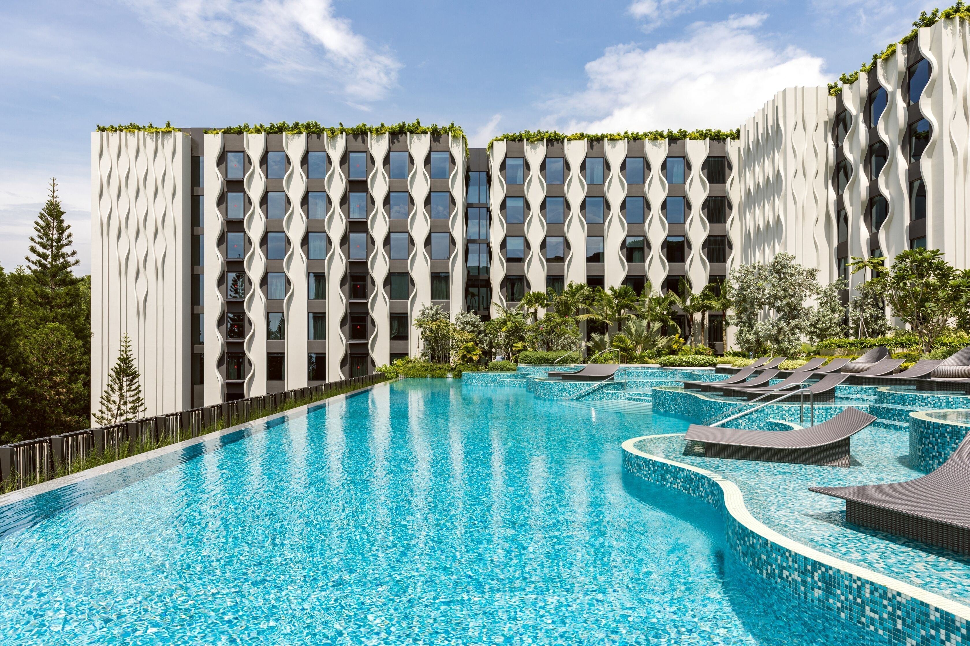 A modern hotel with a large swimming pool and lounge chairs.