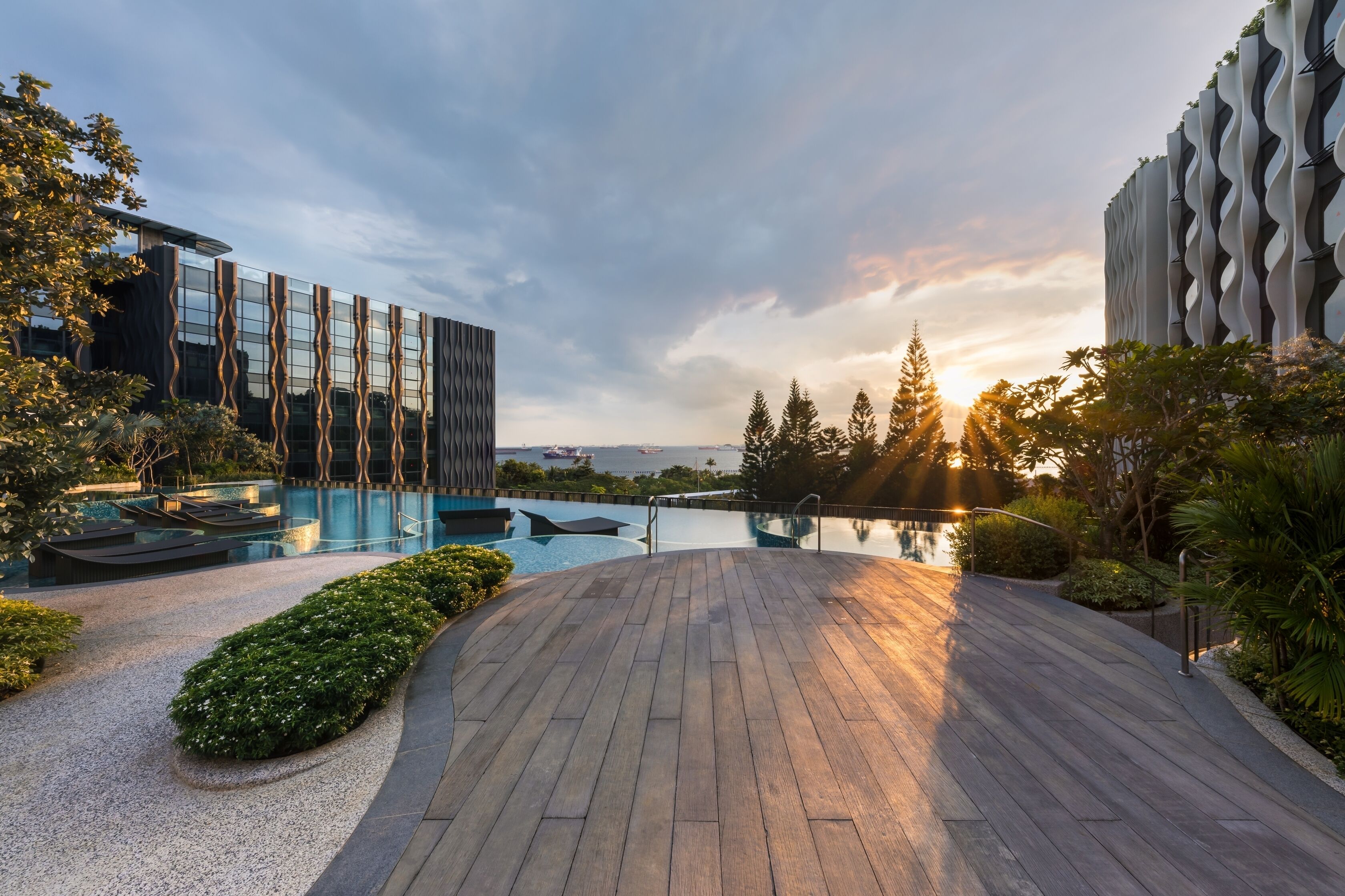 Un hotel moderno con piscina, una terraza de madera y vistas al mar.