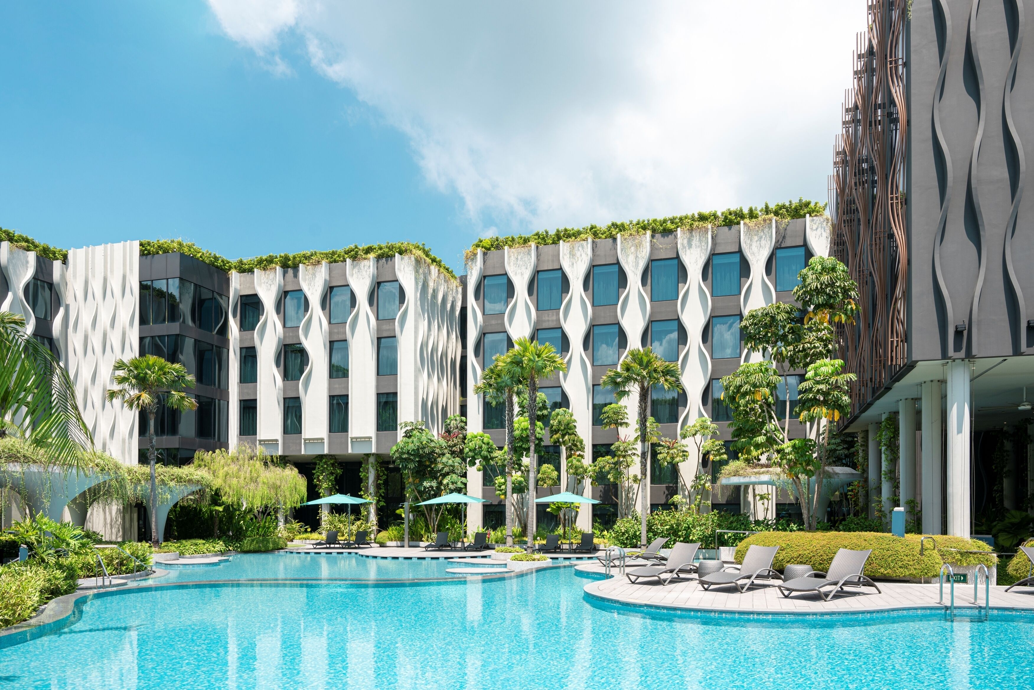A modern hotel with a swimming pool, lounge chairs, and a unique architectural design.