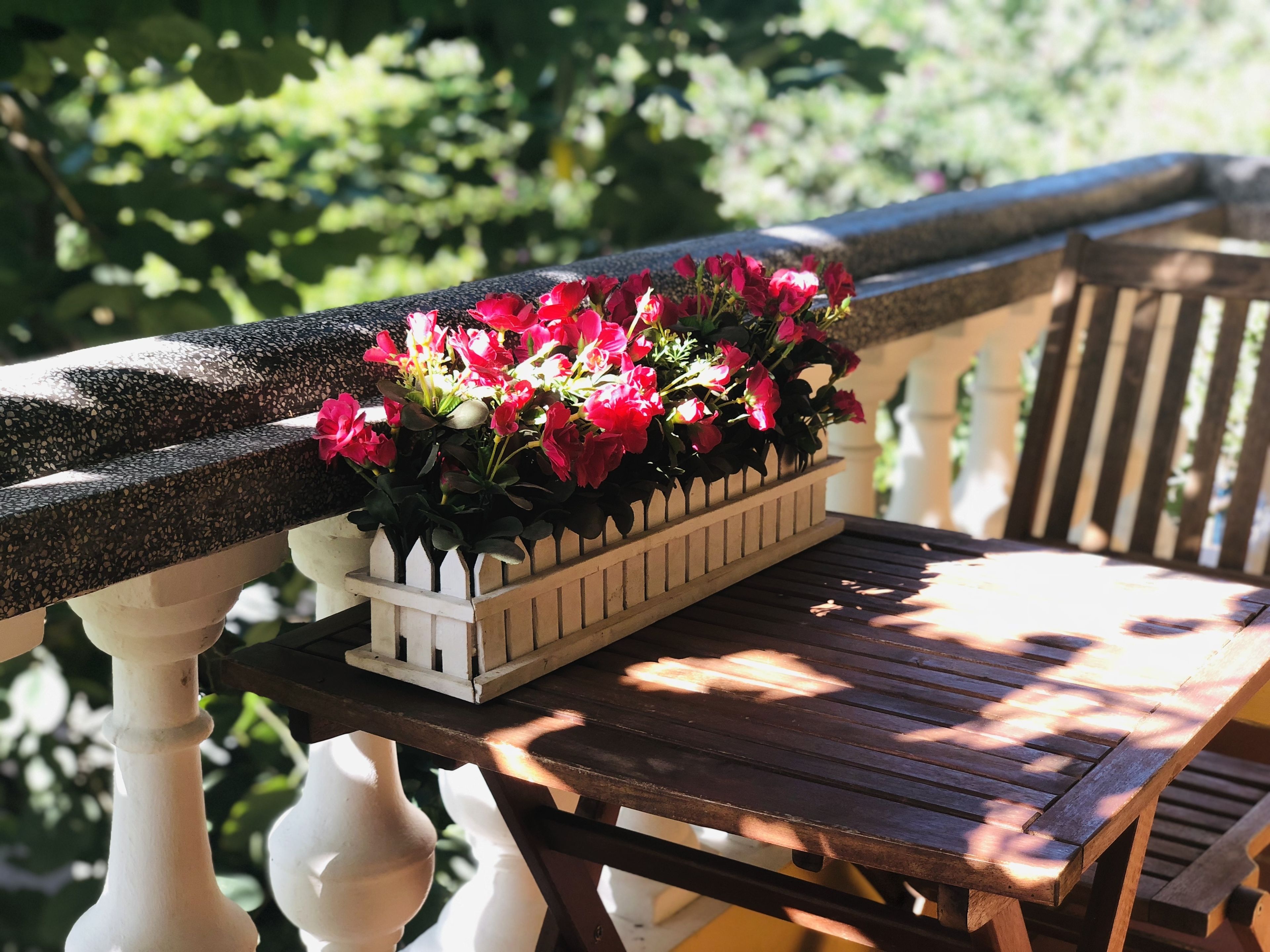 A wooden bench with a planter box containing red flowers on a balcony.