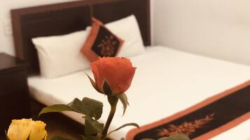 A bed with a white and orange bedspread, a red rose, and a yellow rose in the foreground.