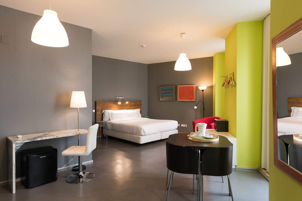 Una habitación de hotel moderna con cama, escritorio, silla y mesa de comedor con bandeja.