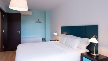 A hotel room with a bed, bedside tables, a hanging light fixture, and a wall-mounted air conditioner.