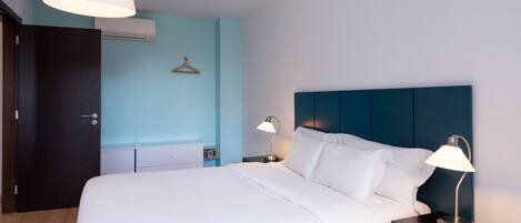 Habitación de hotel con cama, mesitas de noche, lámpara colgante y aire acondicionado instalado en la pared.