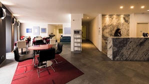 Un moderno vestíbulo de hotel con mostrador de recepción, zona de estar con mesas y sillas, y una pared decorativa de mármol.