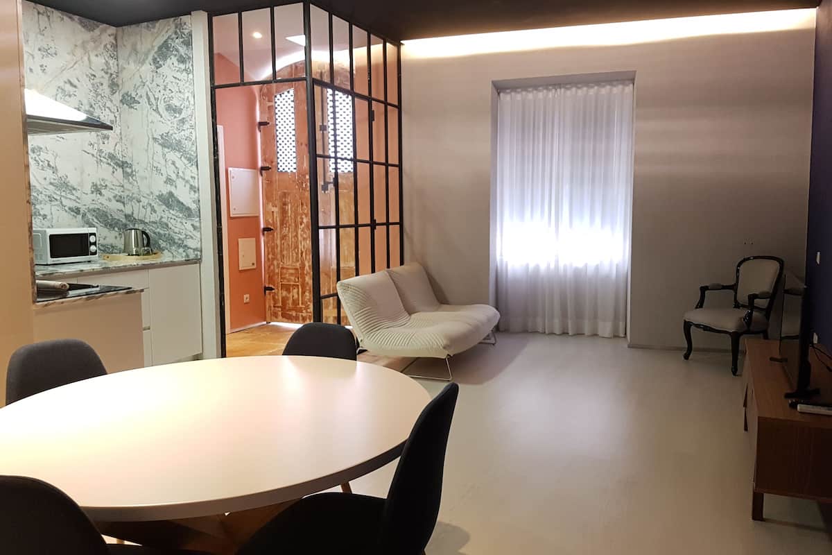 Una sala de estar moderna con una mesa de comedor redonda, un sofá y una silla. Hay una zona de cocina con microondas y hervidor.