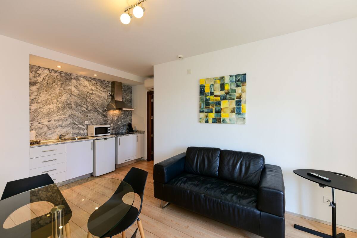 Un espacio habitable moderno con cocina, un sofá de cuero negro y una zona de comedor.