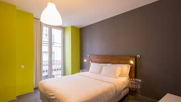 Une chambre d’hôtel avec un lit, une table de chevet, un luminaire suspendu et une vue sur le balcon extérieur.