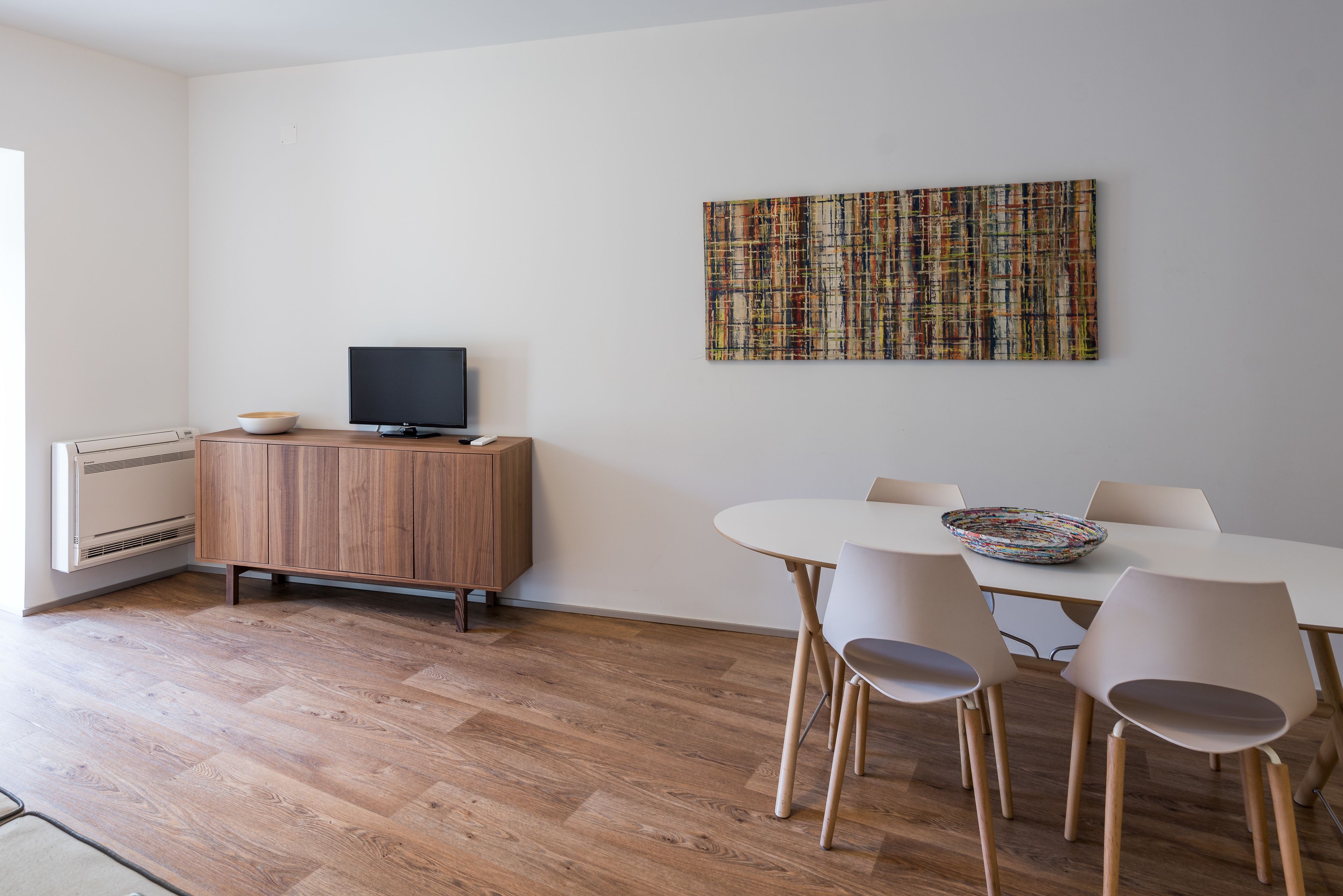 Un espace repas moderne avec un meuble en bois, un téléviseur à écran plat et un tableau abstrait aux couleurs vives accroché au mur.