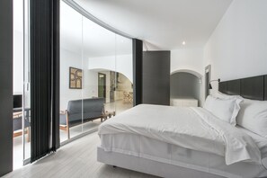 Een moderne slaapkamer met een groot bed, een glazen deur naar een balkon en uitzicht op de woonruimte.