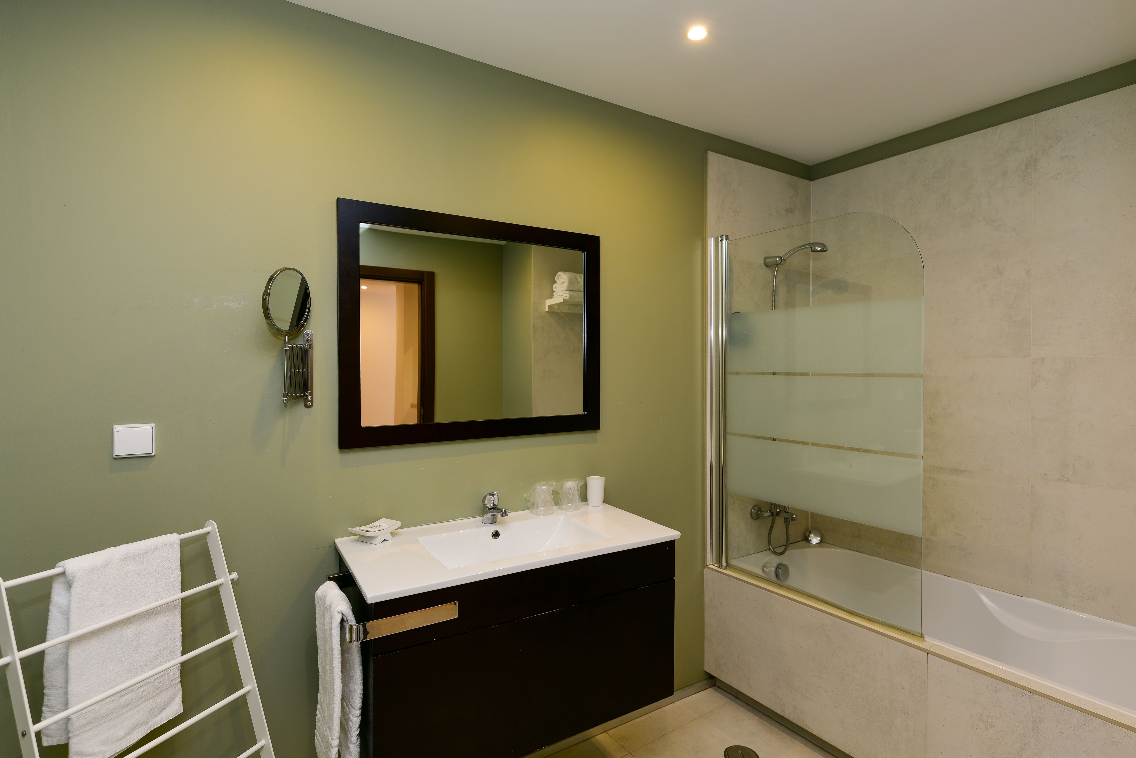 Une salle de bain moderne avec un lavabo blanc, un meuble-lavabo foncé, un grand miroir et une douche à parois de verre.
