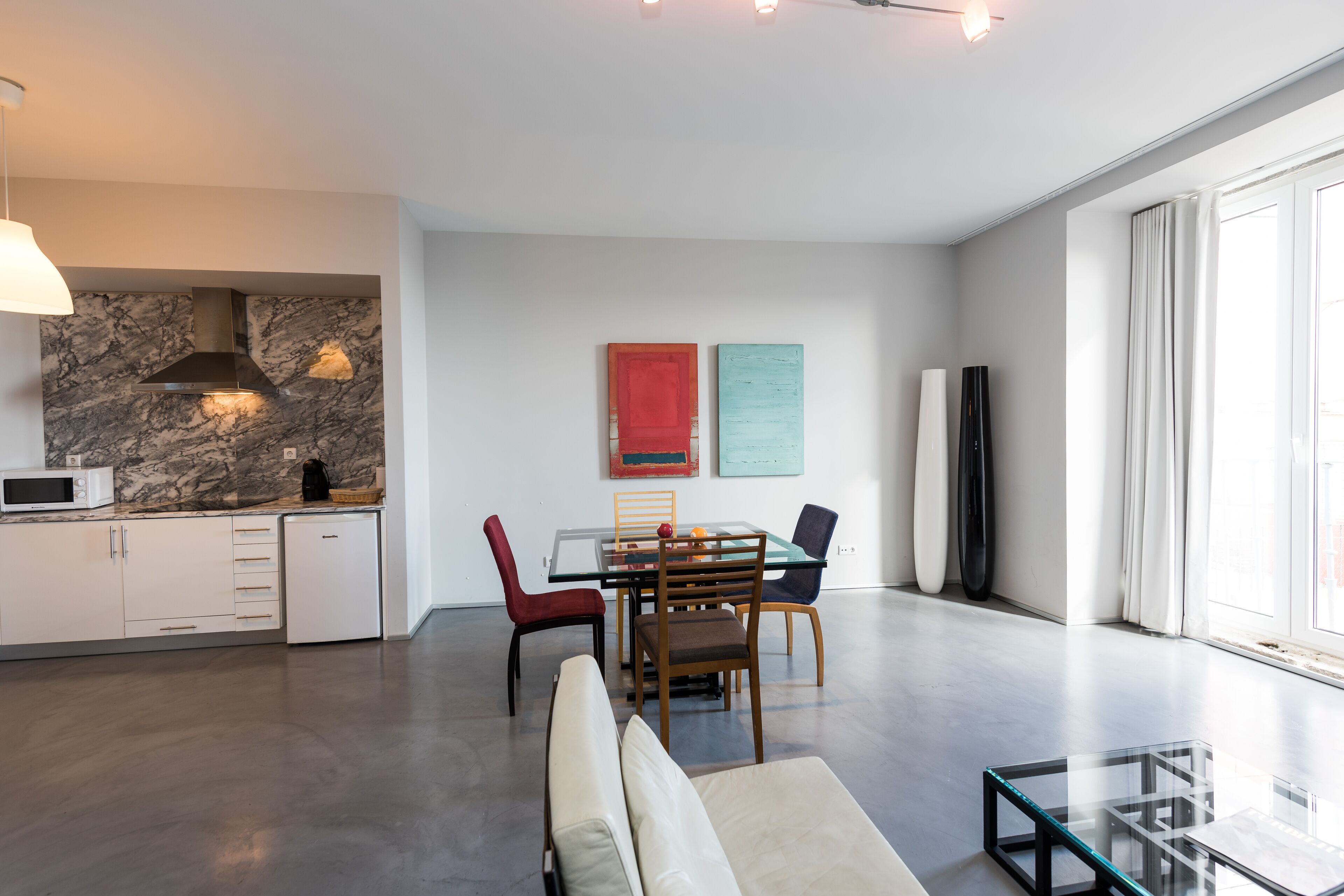 A modern kitchen with a marble backsplash, a dining area with a glass table, and a large window providing natural light.