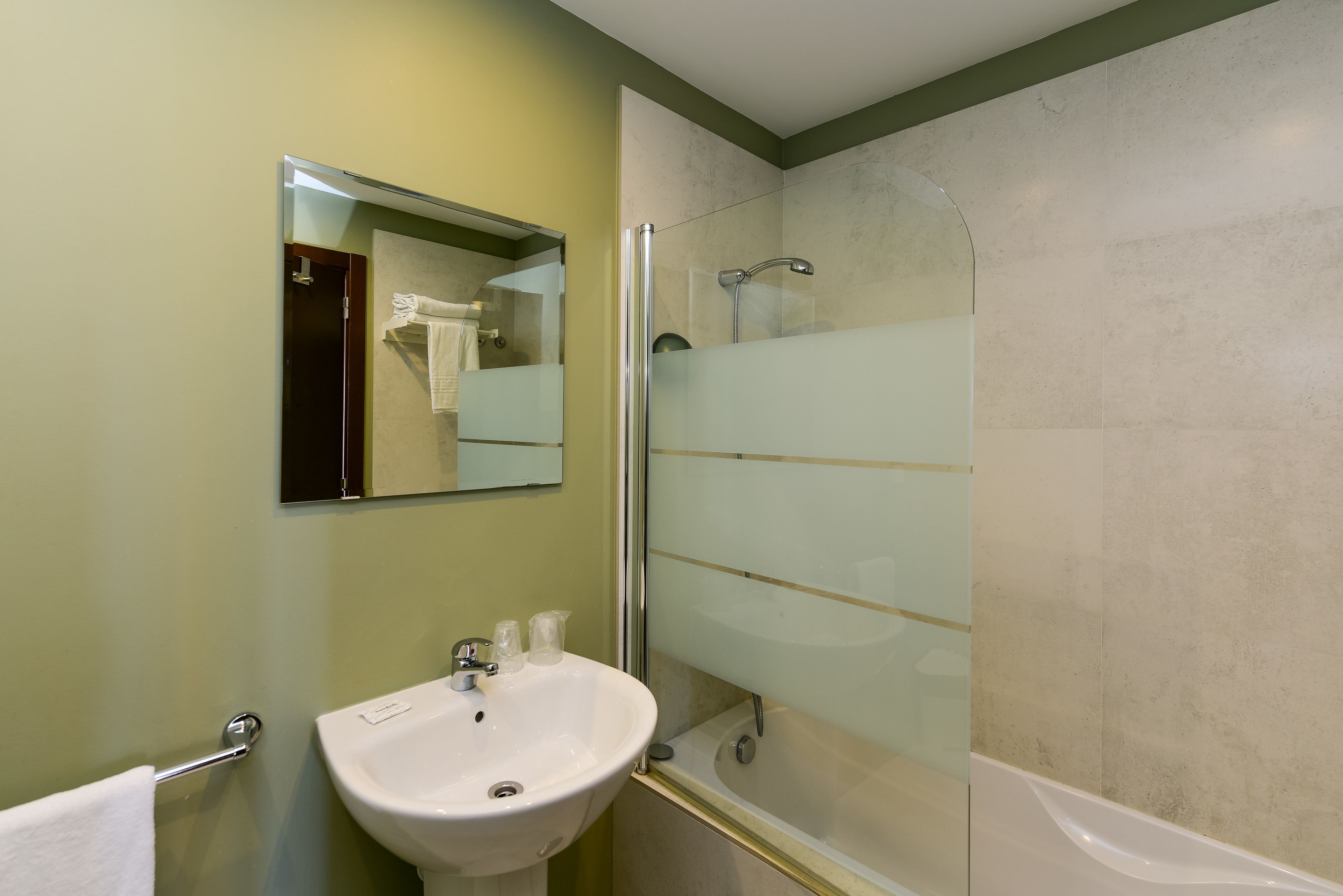 Een badkamer met een douche met glazen wand, een wastafel en een spiegel.