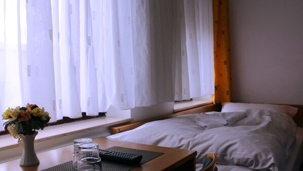 A hotel room with a bed, a bedside table with a vase of flowers, a remote control, and a window with white curtains. - Landgasthaus Veltheimer Hof (Porta Westfalica)
