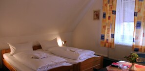 A room with two beds, a small table with a vase and remote controls, and a window with curtains. - Landgasthaus Veltheimer Hof (Porta Westfalica)