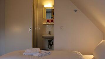 A hotel room with a bed, a bathroom visible through an open door, and a small shelf with toiletries.