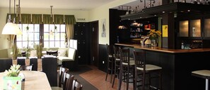 Un área de bar con sillas de madera, una barra con botellas y una cortina verde.