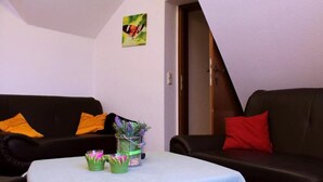 A living room with a black sofa, a white table, and a glass vase with flowers. - Landgasthaus Veltheimer Hof (Porta Westfalica)