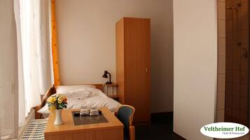 Una habitación de hotel con cama, escritorio con un florero, lámpara y armario.