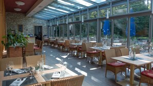 Un restaurant doté d’un toit en verre, de meubles en osier et offrant une vue sur le jardin.
