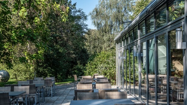 Une terrasse extérieure dotée de meubles en osier et de murs en verre donnant sur un jardin.