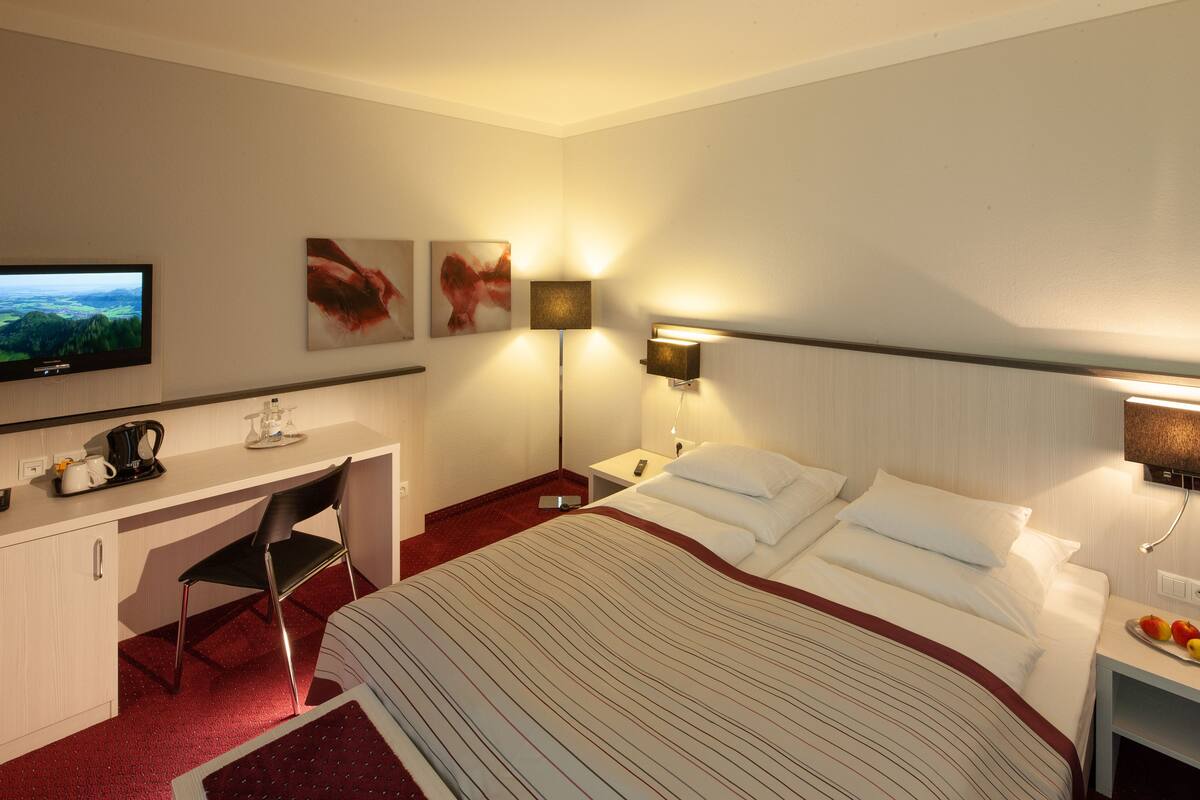 Una habitación de hotel con cama, escritorio, silla, televisión y obras de arte en la pared.