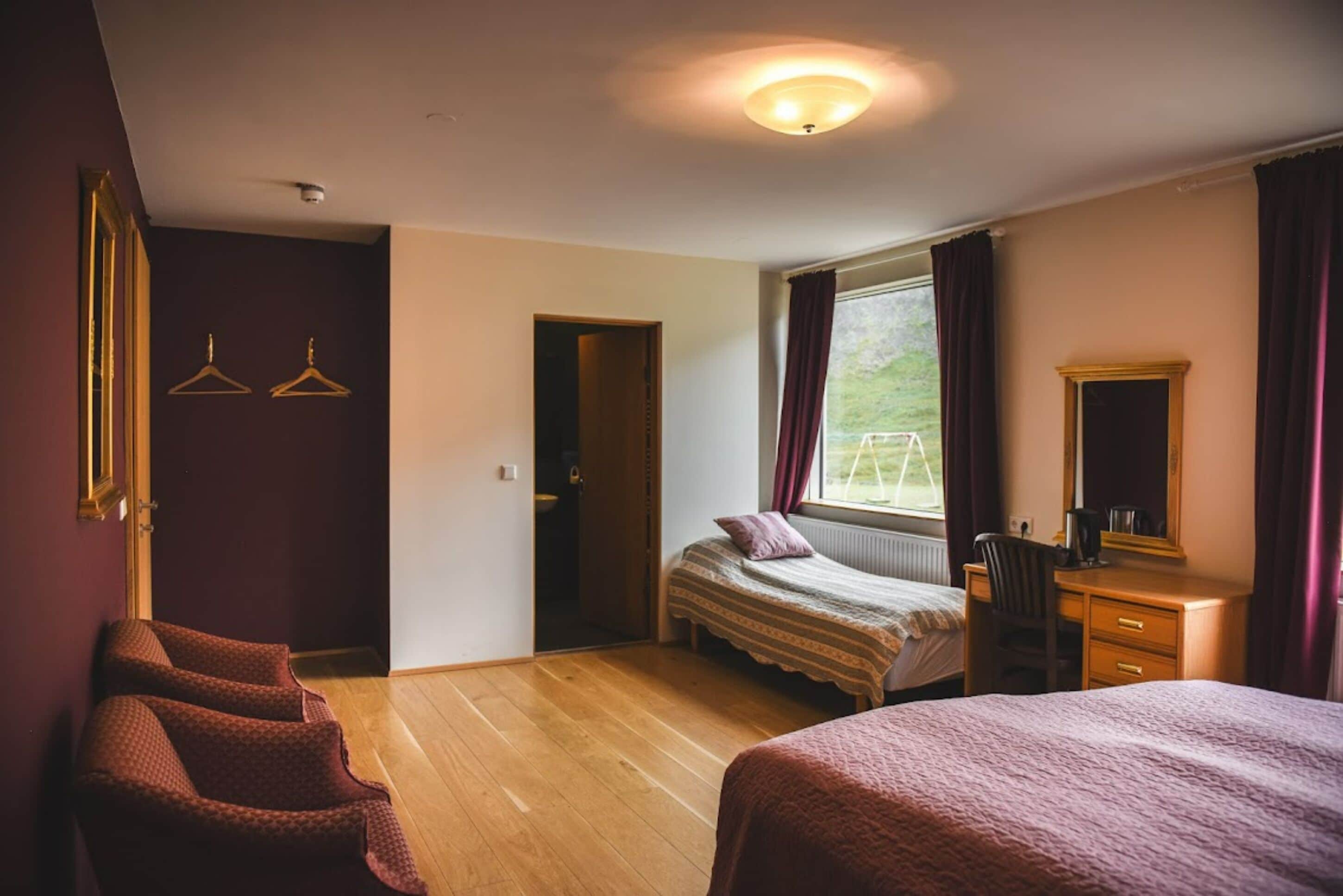 A bedroom with a bed, a desk, a chair, and a window with curtains.