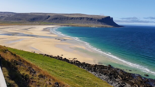Un paisaje costero con una playa arenosa, un litoral rocoso y un acantilado al fondo.
