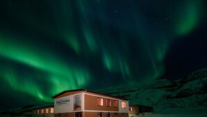 Un hotel con un cartel que dice "Hotel & Låtrabjarg" en un paisaje nevado bajo un cielo estrellado con auroras boreales visibles.