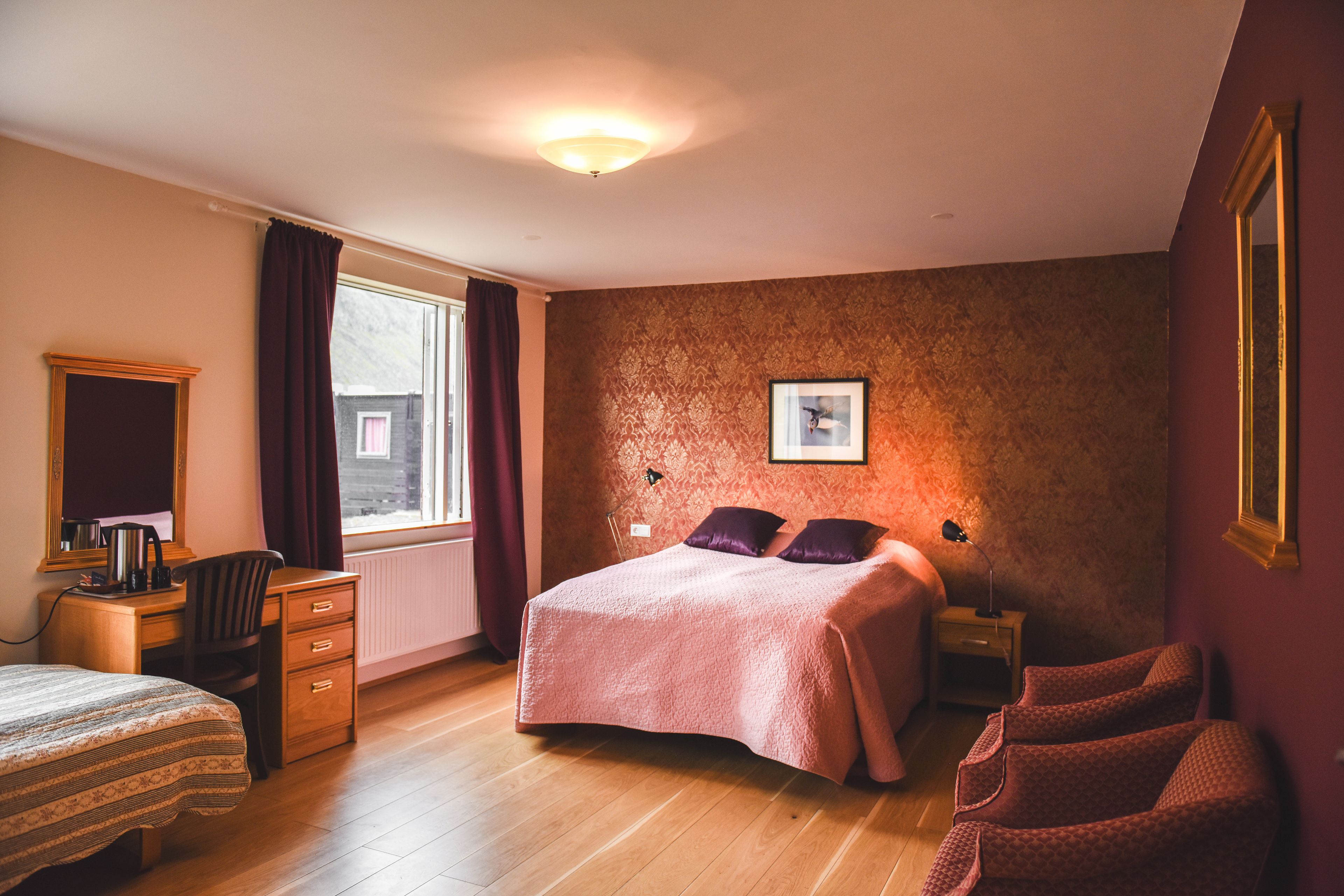 A bedroom with a bed, a desk, a chair, a dresser, a window with curtains, and a framed picture on the wall.