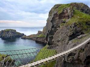 Paisagem costeira com uma ponte suspensa, falésias rochosas e mar calmo.