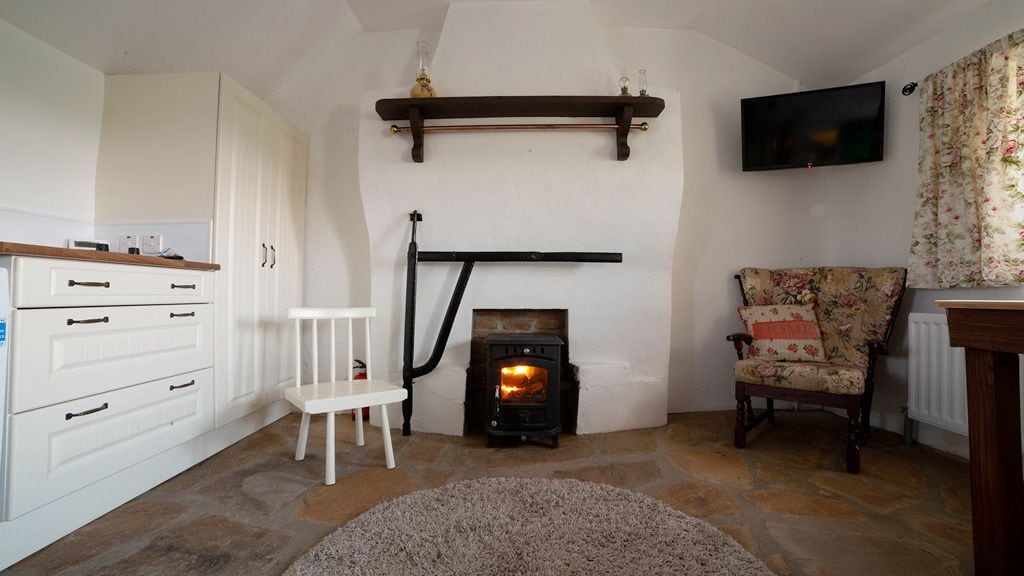 A cozy living room with a stone fireplace, white cabinetry, a white chair, and a floral armchair.