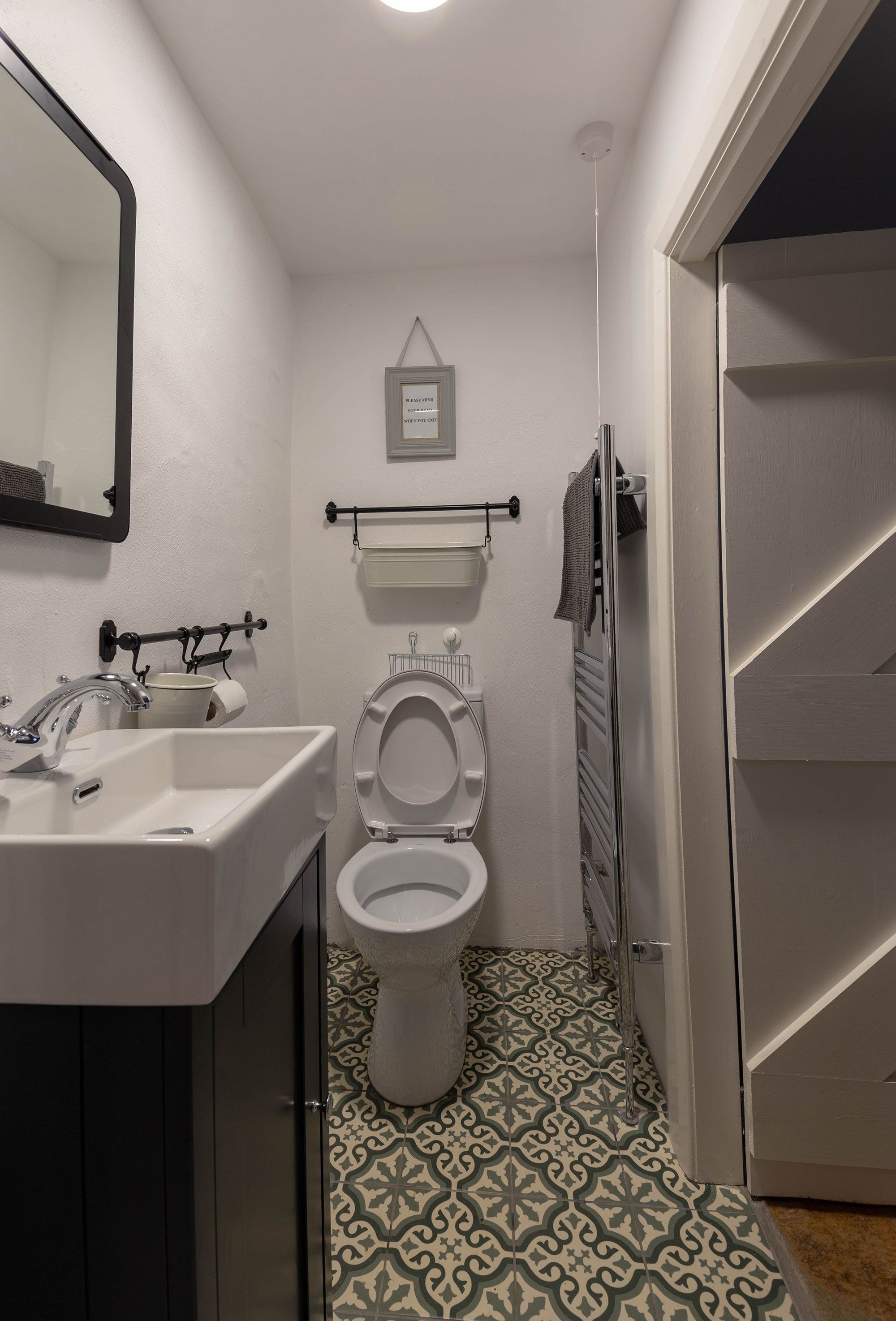 A bathroom with a white sink, mirror, toilet, and patterned floor tiles.