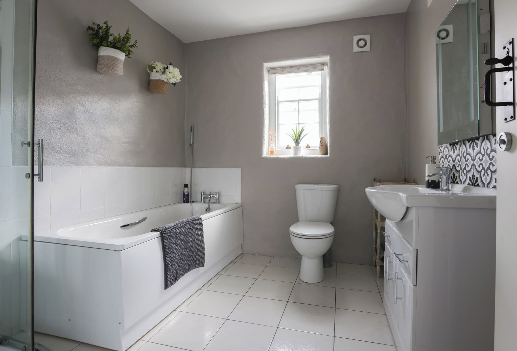Een badkamer met bad, toilet en wastafel. Er is een raam voor natuurlijk licht en een spiegel boven de wastafel.
