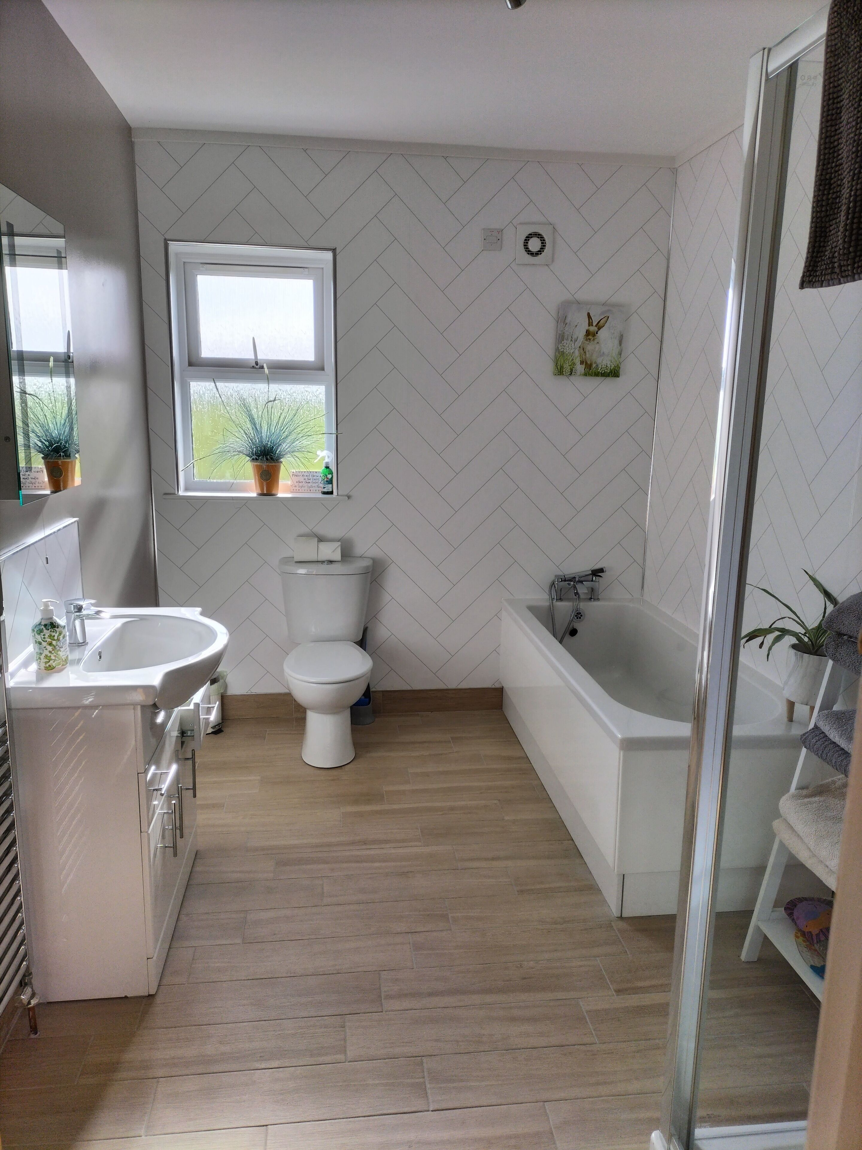 A modern bathroom with a white herringbone-patterned wall, a freestanding bathtub, a toilet, and a sink with a mirror.