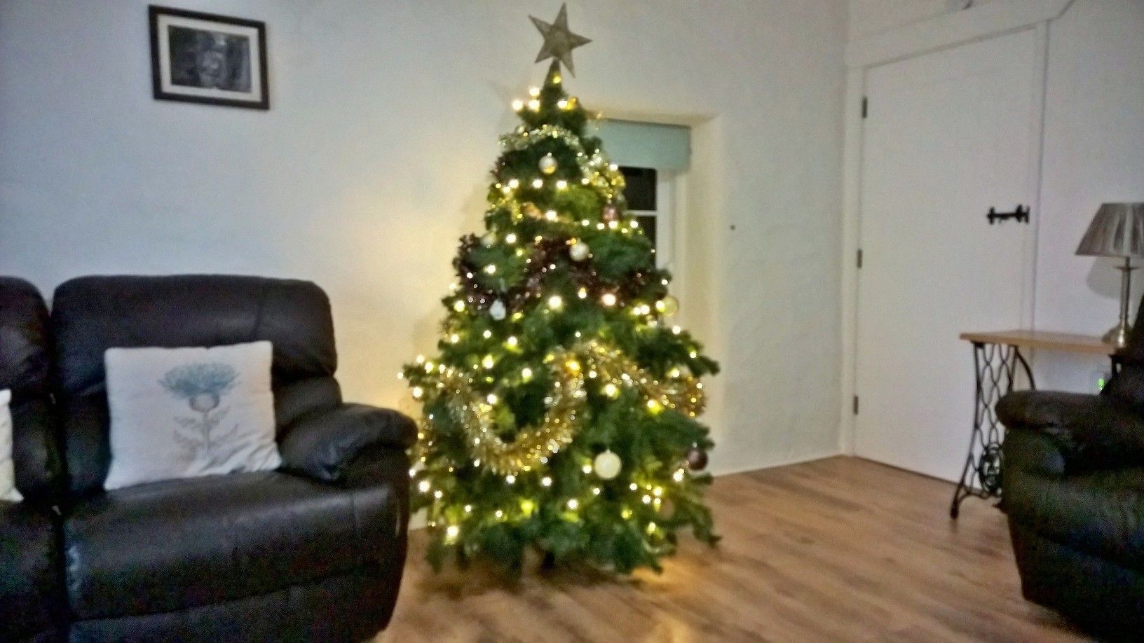 Un salon avec un sapin de Noël, des fauteuils en cuir et une lampe.